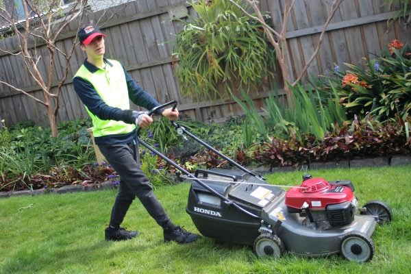 A young man in a baseball cap and high-vis vest mowing the lawn